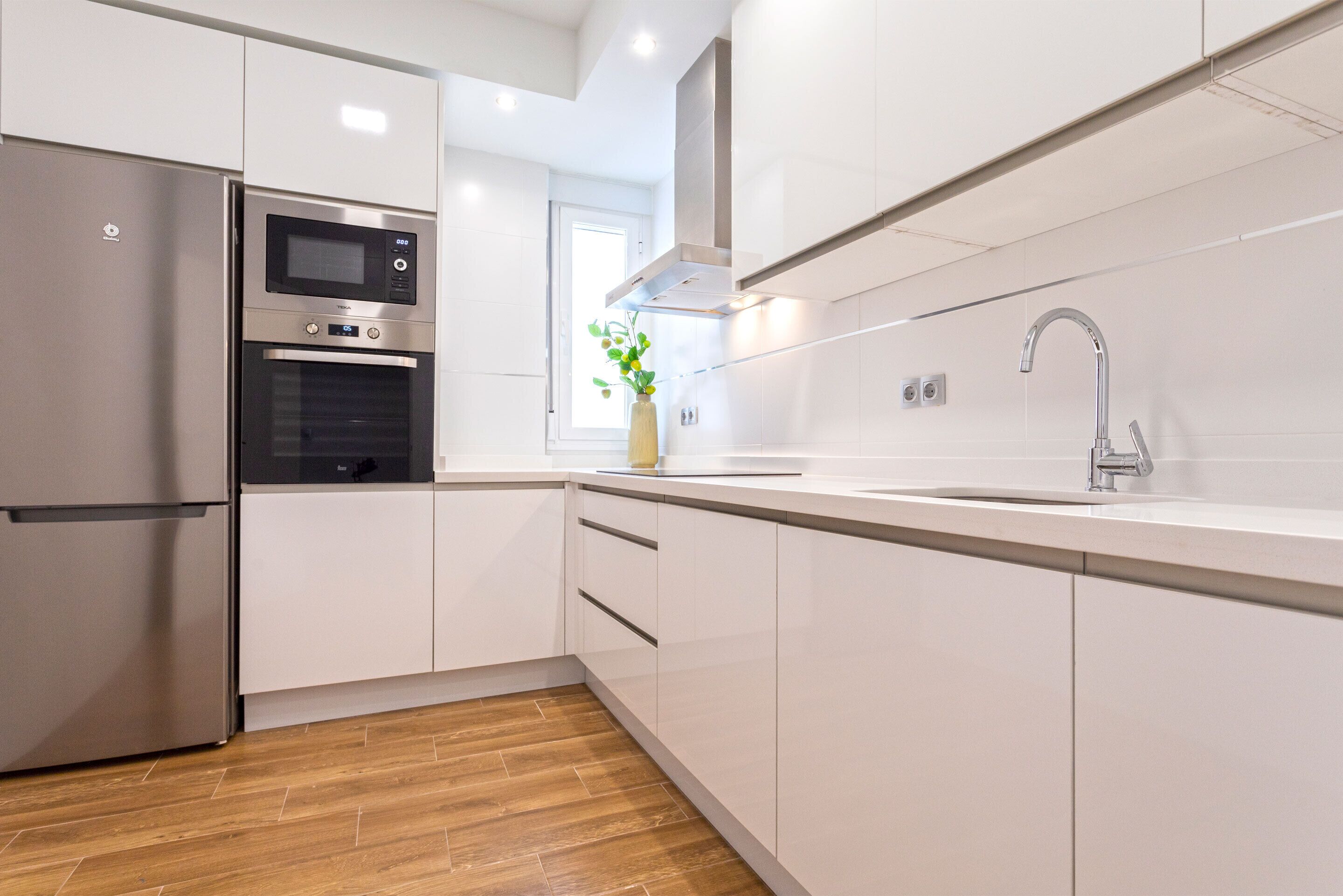 A modern kitchen with white cabinetry, a stainless steel refrigerator, a built-in oven, a microwave, and a sink with a modern faucet.