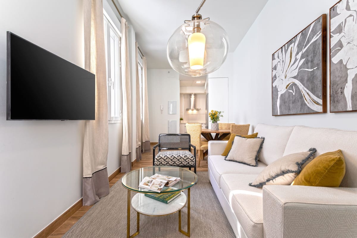 Un salon moderne avec un téléviseur à écran plat, une table basse en verre, un canapé et un coin repas à l’arrière-plan.