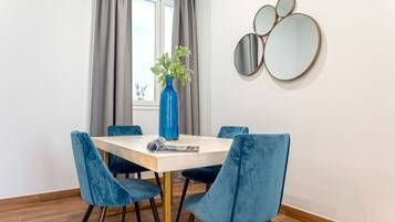 Un comedor con una mesa de madera, cuatro sillas de terciopelo azul, un jarrón azul con plantas verdes y tres espejos redondos en la pared.