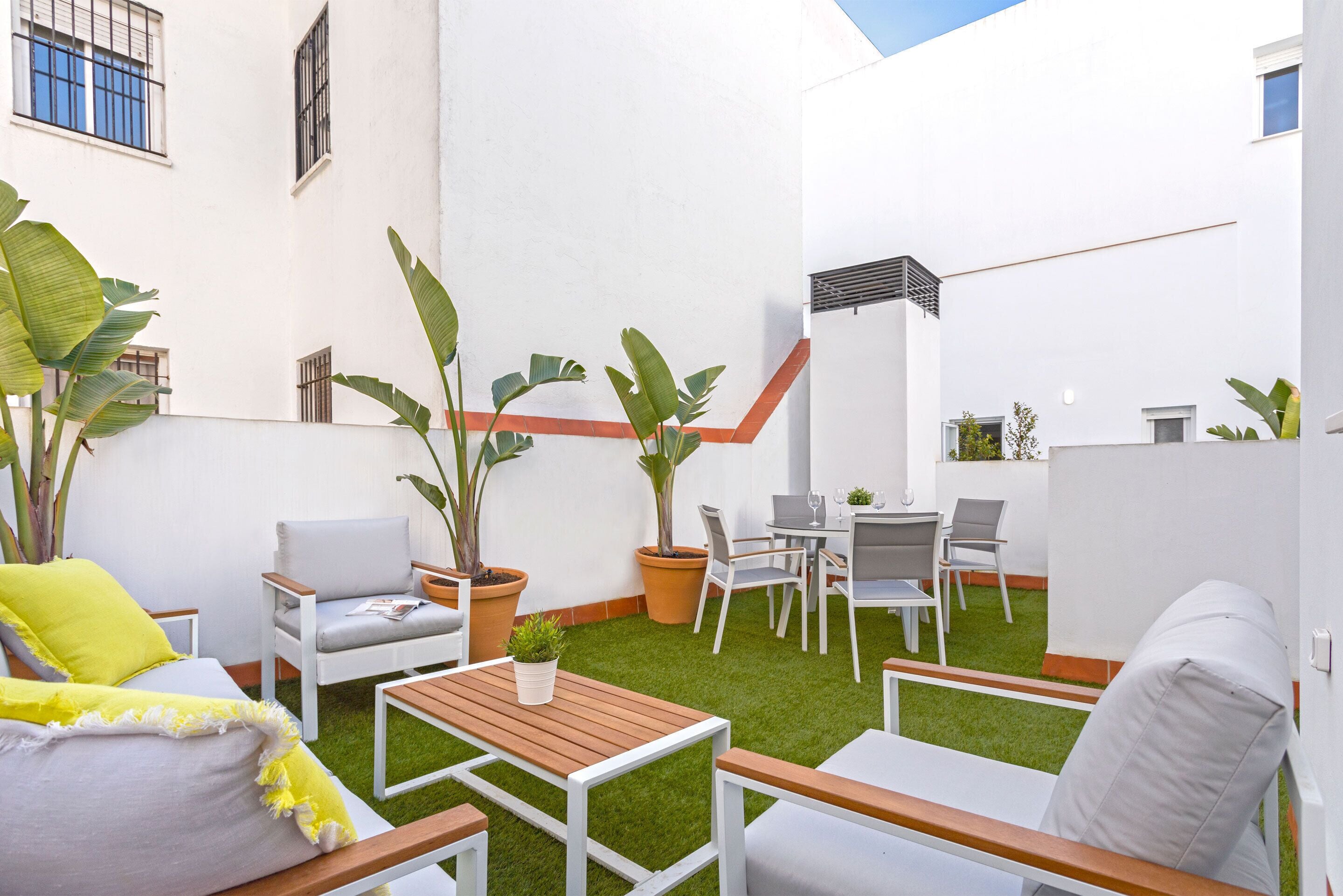 Un patio con muebles blancos, césped artificial verde y plantas en macetas.
