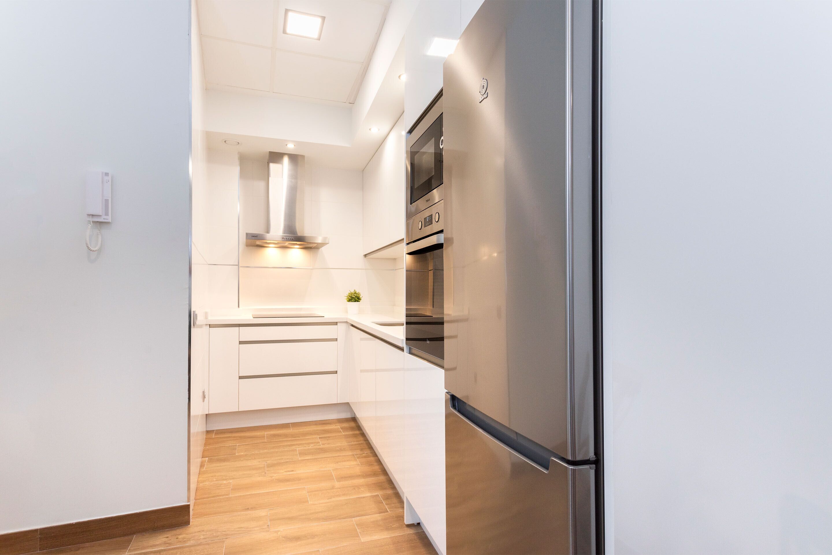 A modern kitchen with white cabinets, a stainless steel refrigerator, and a built-in oven.