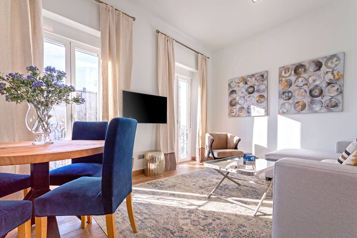 Un salon moderne avec une table à manger en bois, des chaises bleues, un canapé beige et une table basse en verre.