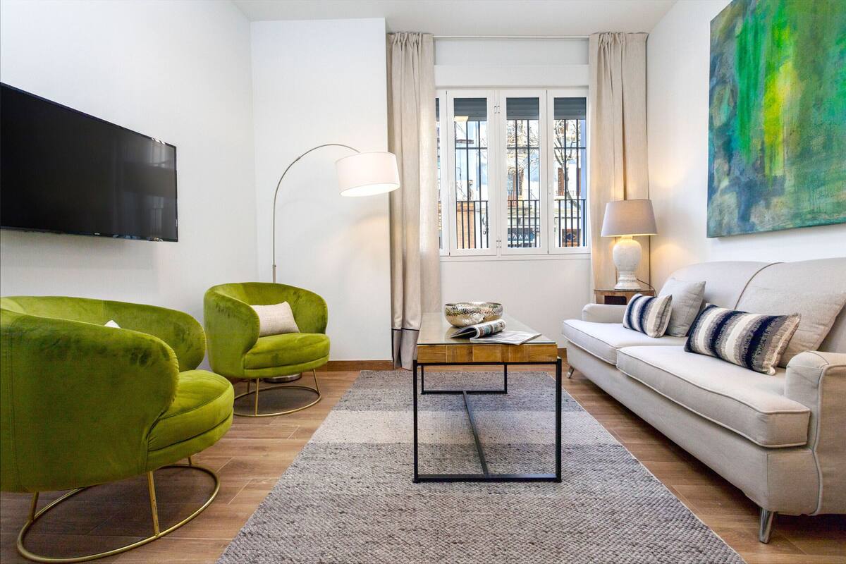 Un salon moderne avec un téléviseur à écran plat, deux fauteuils verts, un canapé beige et une table basse.