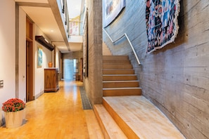 Eine Holztreppe führt zu einer zweiten Etage, einem Flur mit Holzdielen und einem großen Topfpflanzen mit roten Blüten.