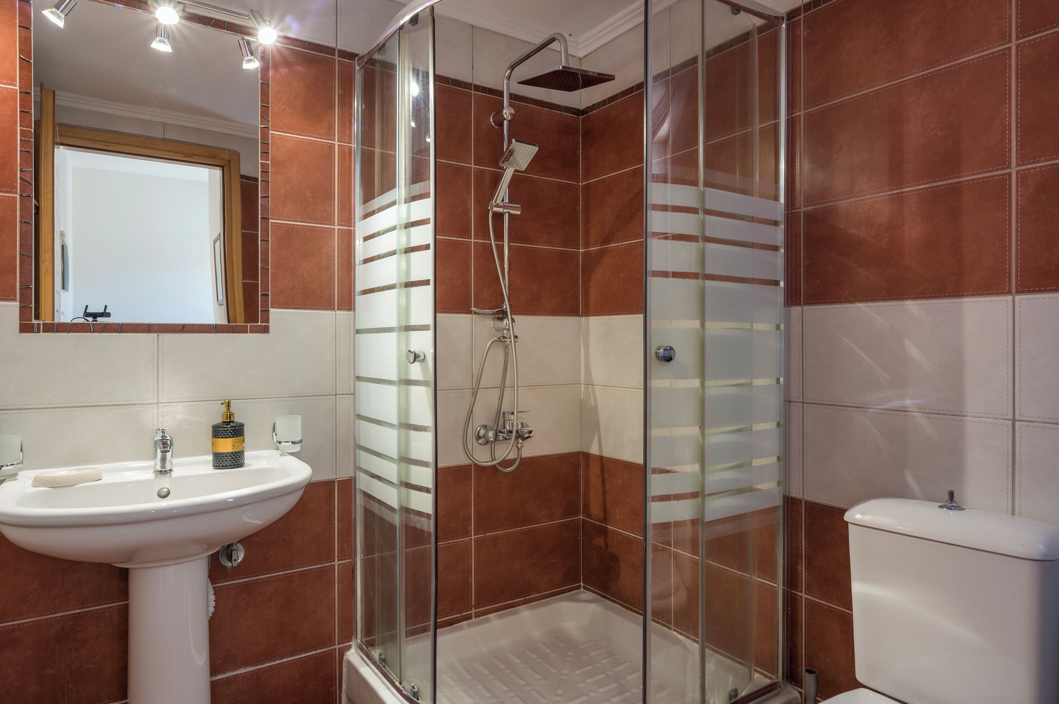 A bathroom with a glass-enclosed shower, a white sink, and a toilet.