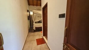 Een smalle gang met een houten deur aan de rechterkant, die leidt naar een kamer met een bed en hemelbed.