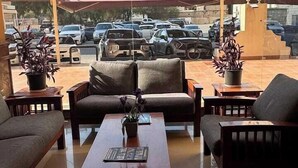 Zona relax esterna coperta con divani e tavolino, con vista su un parcheggio e edifici.