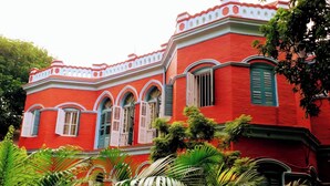 A red building with arched windows and a white trim. - Urban Trippers Lal Bari Heritage Arindam (Kolkata)