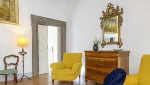A room with a yellow armchair, a wooden dresser, a mirror, and a lamp. - Cartari Deluxe apartment (Roma)