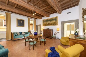 A room with a wooden ceiling, a dining table with chairs, a sofa, a yellow armchair, and a cabinet. - Cartari Deluxe apartment (Roma)
