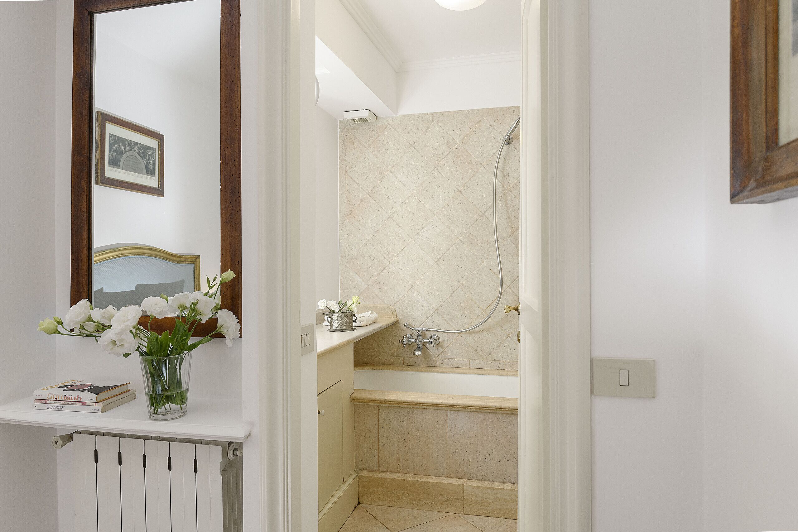 Ein Badezimmer mit einer Badewanne, einer Dusche und einem kleinen Regal mit Büchern und Blumen.