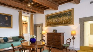 A dining area with a wooden table, chairs, and a vase of flowers. There is a sofa and a lamp in the background. - Cartari Deluxe apartment (Roma)