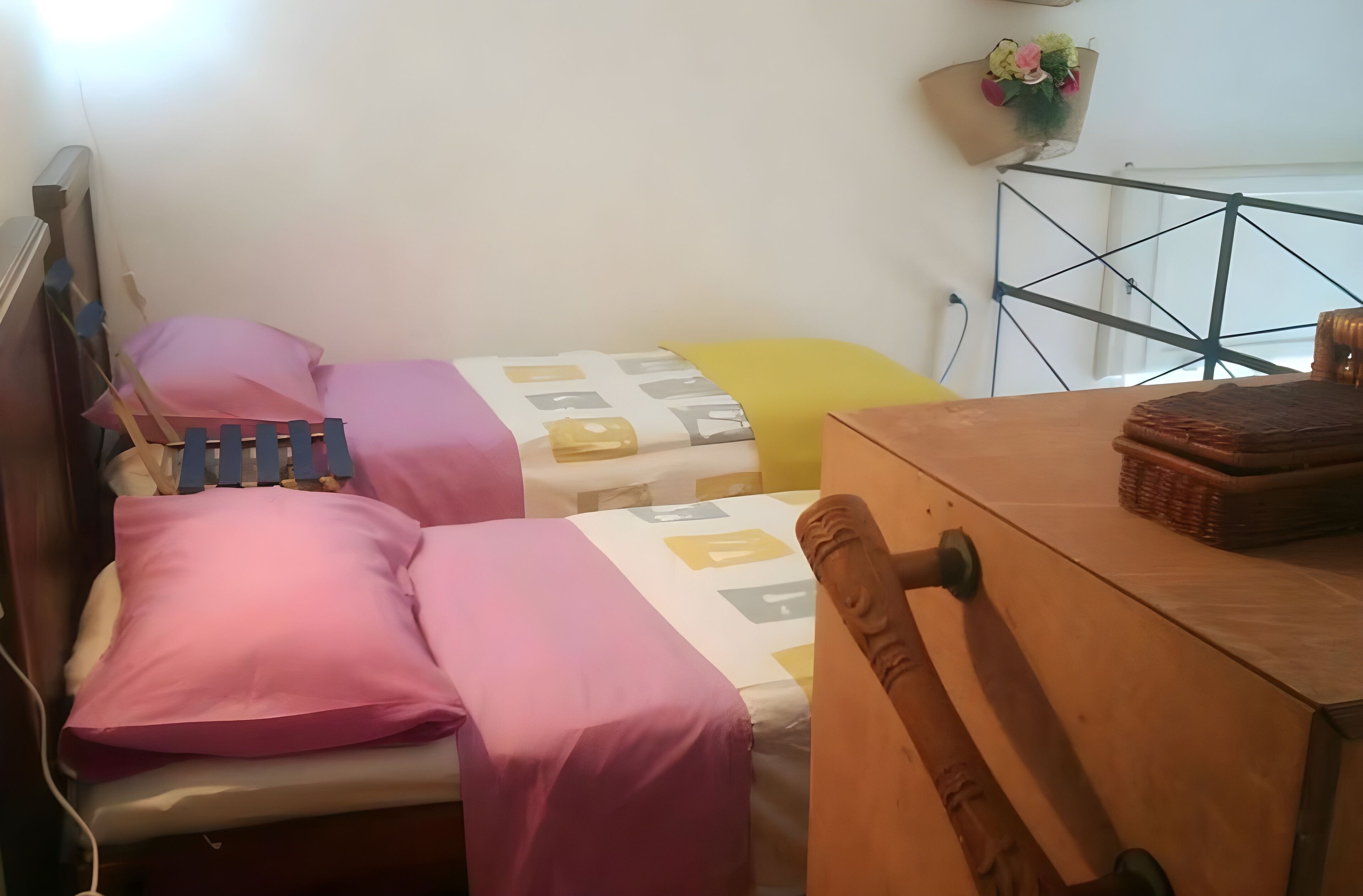 A bedroom with two beds, each with pink and yellow bedding. There is a wooden nightstand with a basket on it.