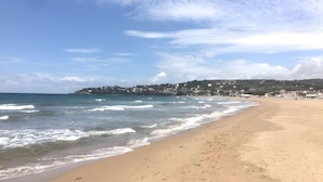 Ein Strand mit Wellen, einem klaren Himmel und Gebäuden im Hintergrund.