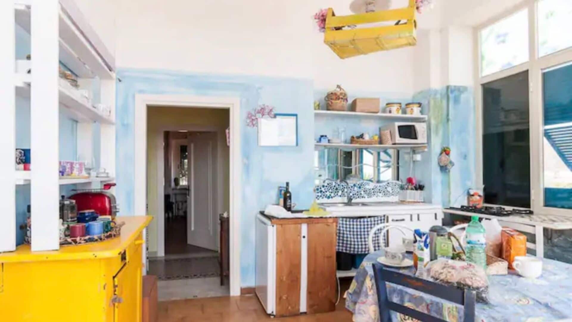 Cozinha compacta com armário amarelo, micro-ondas e pia. Há uma porta de entrada para outro quarto.