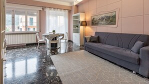 Un soggiorno con un divano grigio, un tavolo da pranzo con sedie, un armadietto bianco e un quadro appeso al muro.