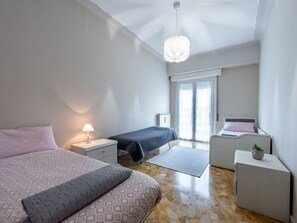 A modern bedroom with two beds, a nightstand with a lamp, a small table with a plant, and a large window with a view. - Lovely apartment for 6 people with WIFI, TV, terrace and pets allowed (Omegna)