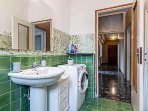 A bathroom with green tiled walls, a white sink, and a washing machine. - Lovely apartment for 6 people with WIFI, TV, terrace and pets allowed (Omegna)