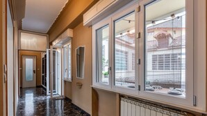 Un corridoio con ampie finestre, un termosifone e una porta che dà su un'altra stanza.