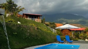 Una piscina con cascata, circondata da un solarium piastrellato e poltrone da relax blu.
