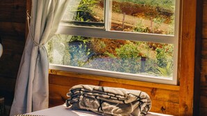 Una camera in una baita di legno con un'ampia finestra, un letto con coperta a righe e vista su un paesaggio verde con una montagna.