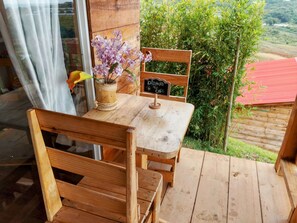 A wooden table and bench set on a balcony with a view of greenery and a red-roofed building. - Glamping Isaju (Ginebra)