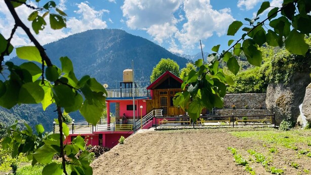 A rustic mountain lodge with a red and yellow exterior, a stone wall, and a view of a mountain range.