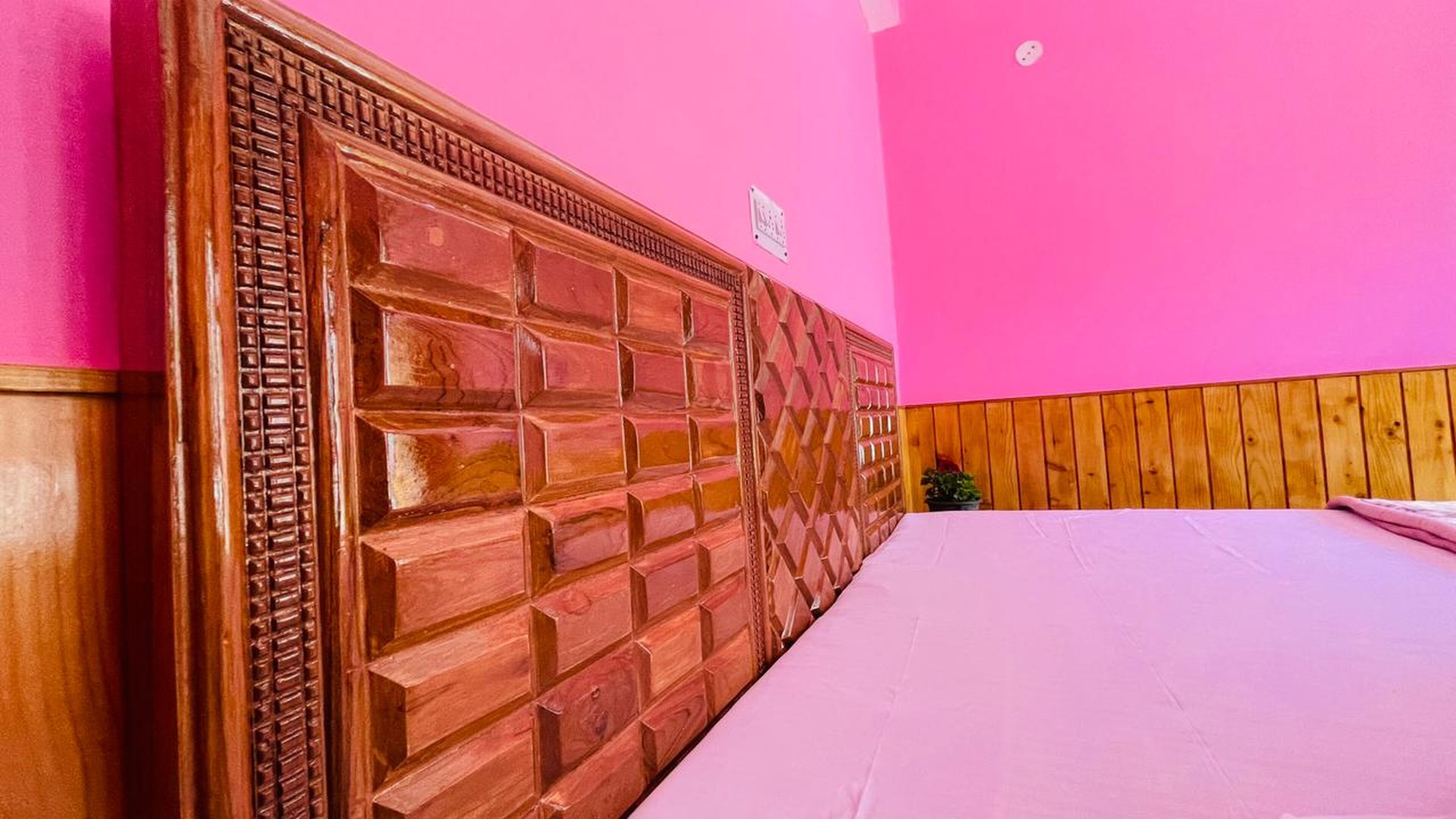Een kamer met een houten hoofdbord, een bed en een roze wand.