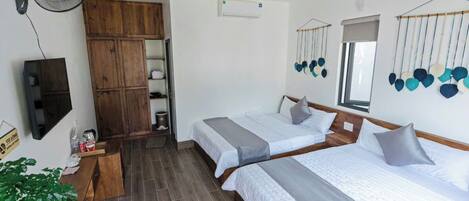 A hotel room with two beds, a wooden wardrobe, a wall-mounted fan, and a TV.