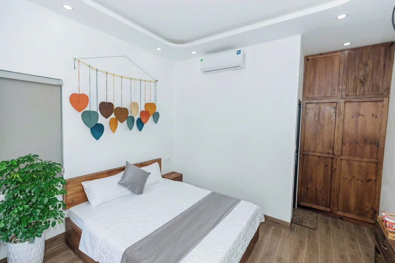 A bedroom with a bed, a wall-mounted heart-shaped decoration, a potted plant, and a wooden wardrobe.
