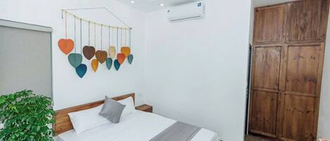 A bedroom with a bed, a wall-mounted heart-shaped decoration, a potted plant, and a wooden wardrobe.