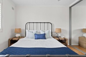A neatly made bed with a headboard, two bedside tables with lamps, and a large mirror on the wall.