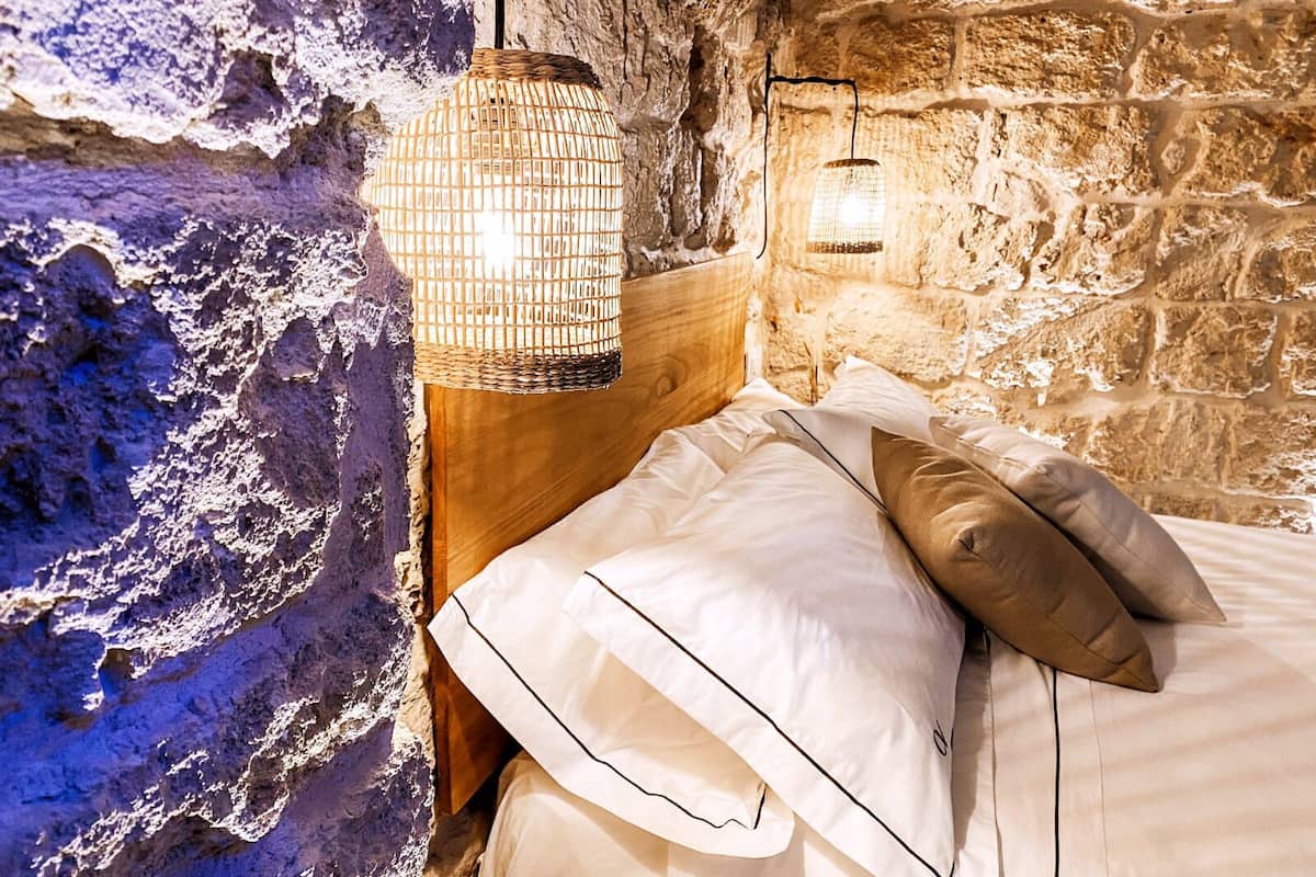 Une chambre rustique avec un mur en pierre, une tête de lit en bois et un luminaire suspendu.