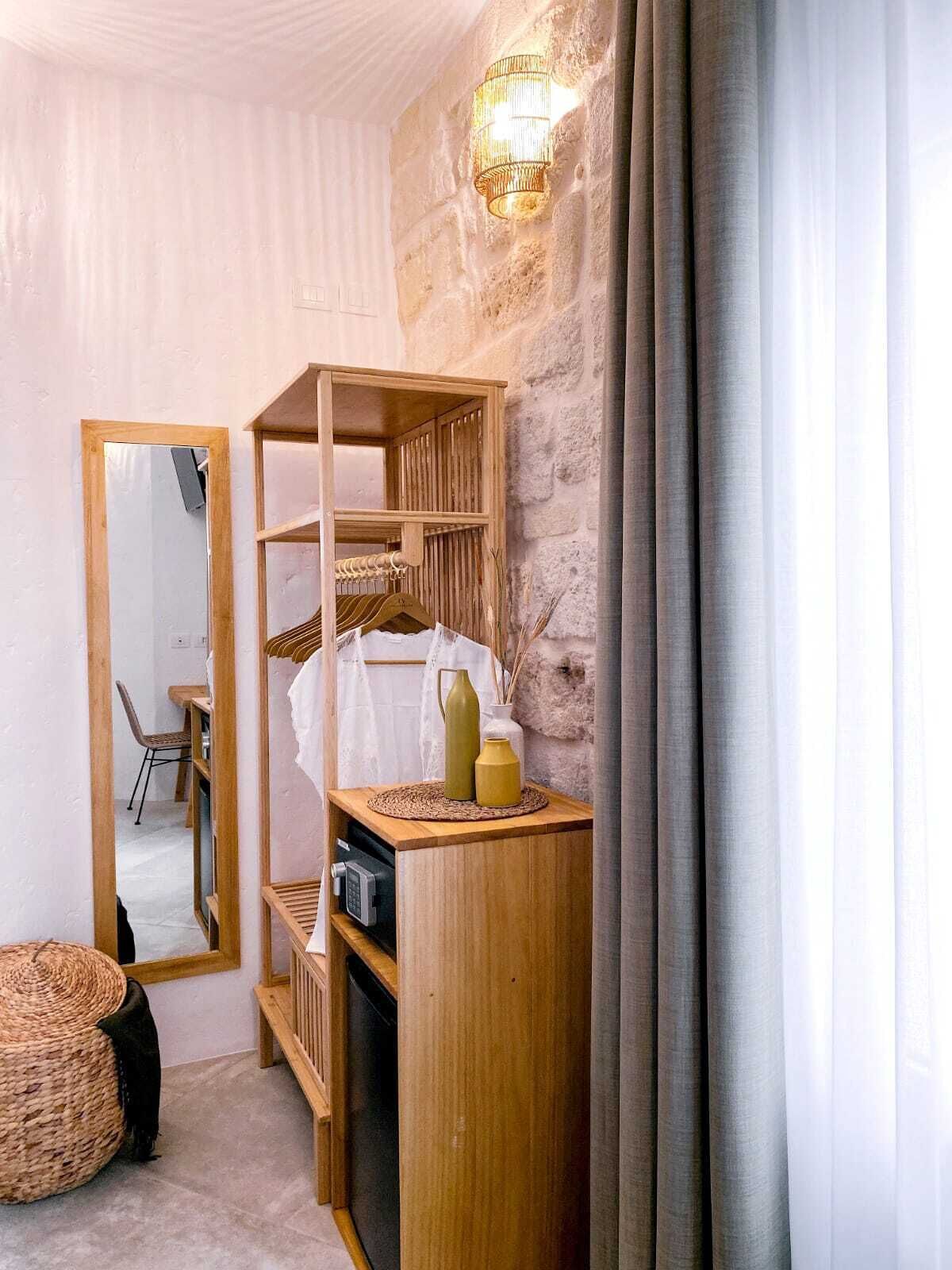 A cozy room with a stone wall, a wooden shelf with a mirror, and a small table with decorative items.