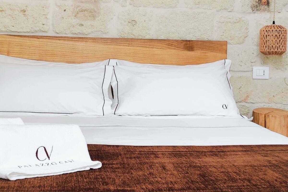 Un lit bien fait, avec des draps blancs, une tête de lit en bois et une décoration murale circulaire en fibres tressées au-dessus.