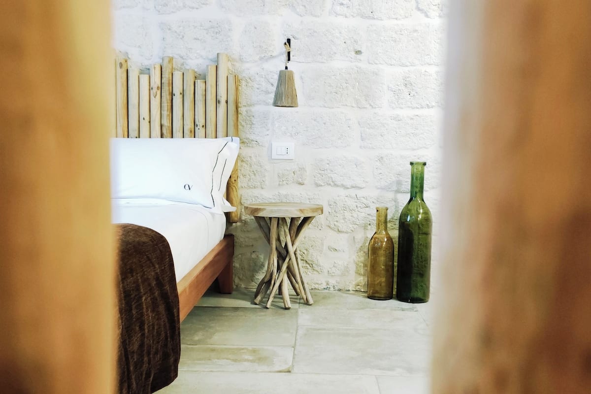 Une chambre à coucher avec un lit, une petite table en bois et deux bouteilles posées sur le sol.