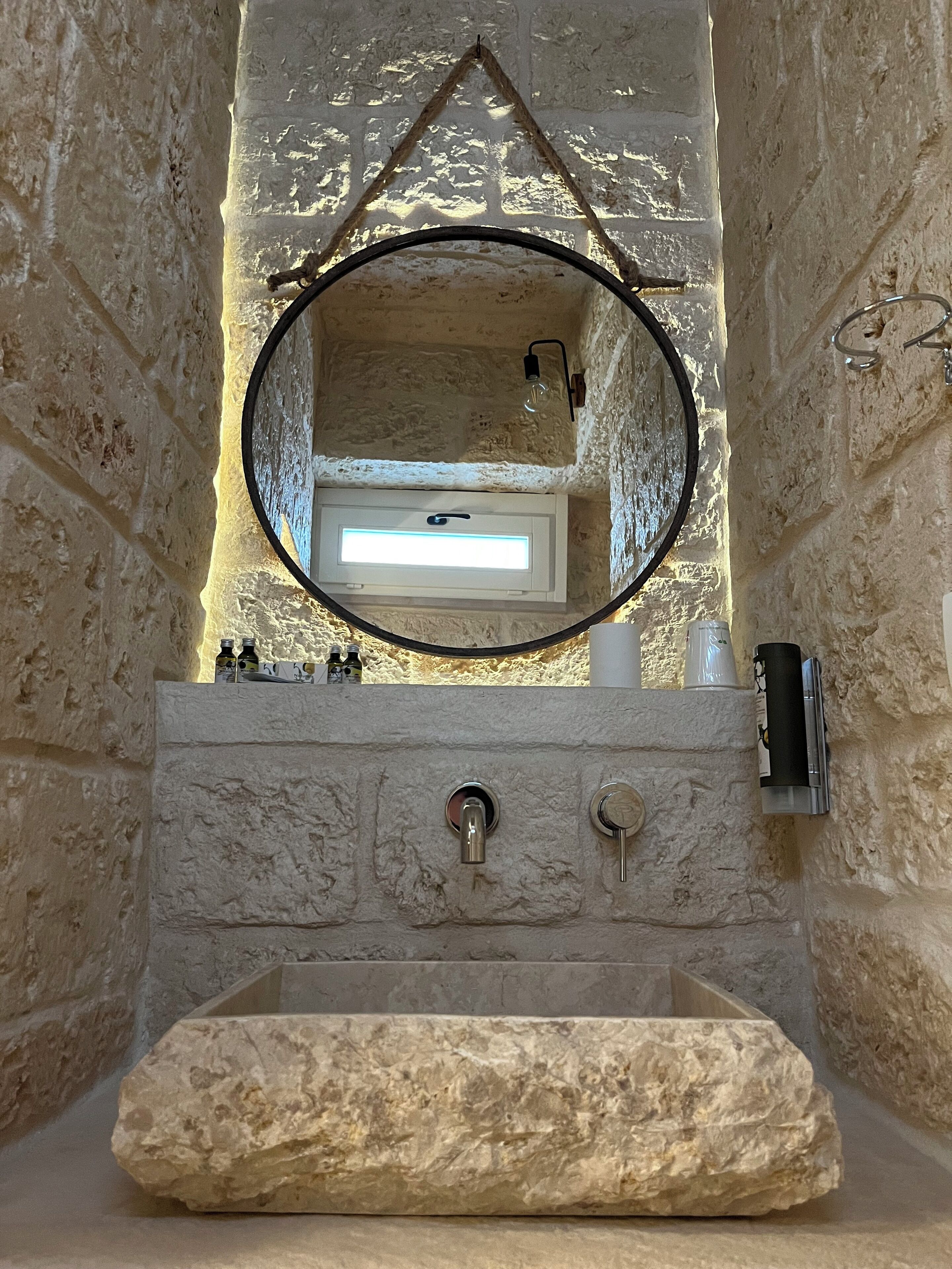 A stone bathroom with a built-in sink, a mirror, and a light fixture above the mirror.