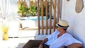 A man relaxing on a sun lounger with a pool and plants in the background. - Palazzo CAVÌ  (Mola di Bari)