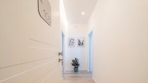 Een gang met een houten vloer, een potplant en twee kunstwerken in lijsten aan de muur.