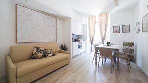 Een moderne woonkamer met een beige bank, een eethoek met een tafel en stoelen, en een keuken op de achtergrond.