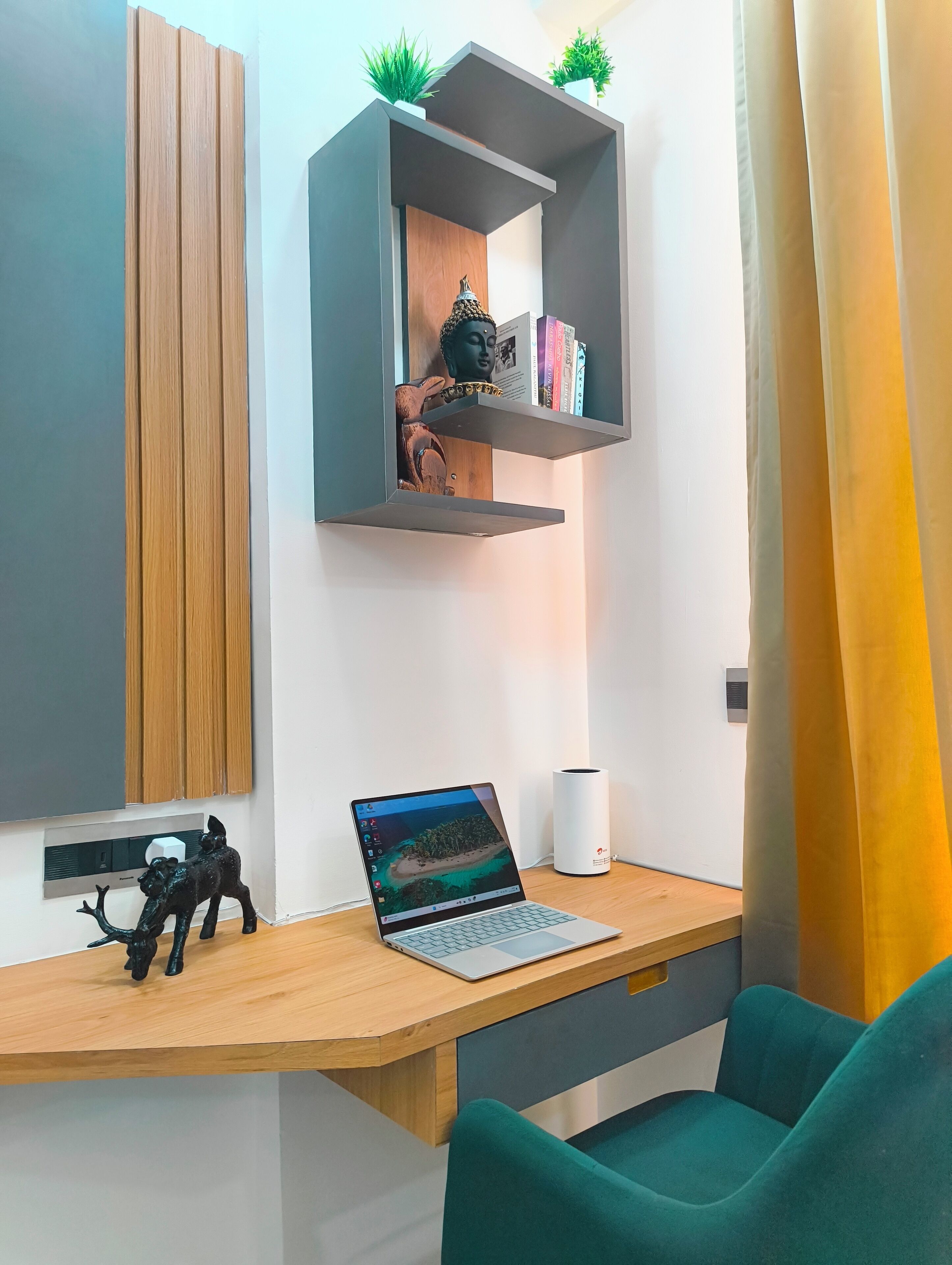 Ein moderner Arbeitsbereich mit einem Holztisch, einem Laptop, einer kleinen Statue und einem Regal mit Büchern und Pflanzen.