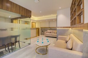 A modern living room with a glass partition, a round coffee table with water bottles, a beige sofa, and a wooden bookshelf. - Mumbai Dorms (Mumbai)