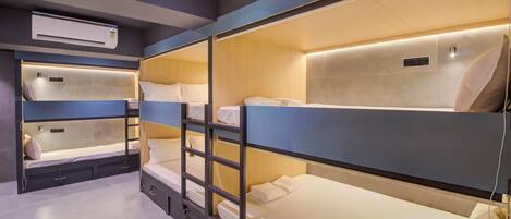 Una habitación de hotel con literas, una mesita de noche, una lámpara y un equipo de aire acondicionado.