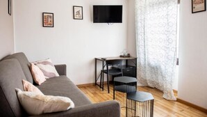 Un salon moderne avec un canapé gris, deux fauteuils noirs, une petite table et un téléviseur à écran plat fixé au mur.