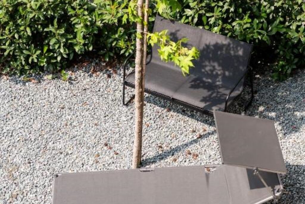 A garden area with a gravel surface, a metal bench, and a tree.