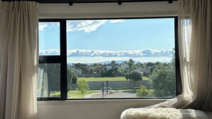 A bedroom with a large window, a bed, a ceiling light, and a view of a landscape with mountains. - Coastal family home, 5 minutes walk to beach, hot tub, fully accessible (Papamoa)