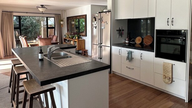 A modern kitchen with a central island, stainless steel appliances, and a dining area with a view. - Coastal family home, 5 minutes walk to beach, hot tub, fully accessible (Papamoa)