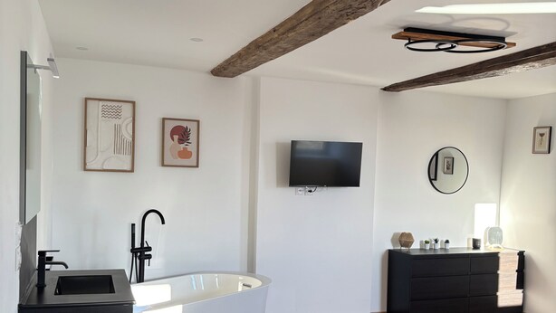Une salle de bain moderne avec une baignoire sur pieds, un meuble-lavabo noir et une poutre en bois au plafond.