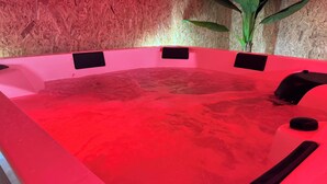 Un bain à remous rouge avec des sièges noirs et une plante en arrière-plan.