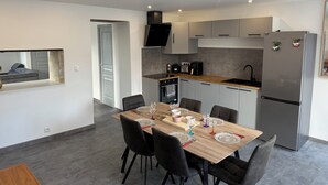 Une cuisine moderne avec un coin repas, comprenant une table en bois avec des chaises, un four encastré et un réfrigérateur en acier inoxydable.